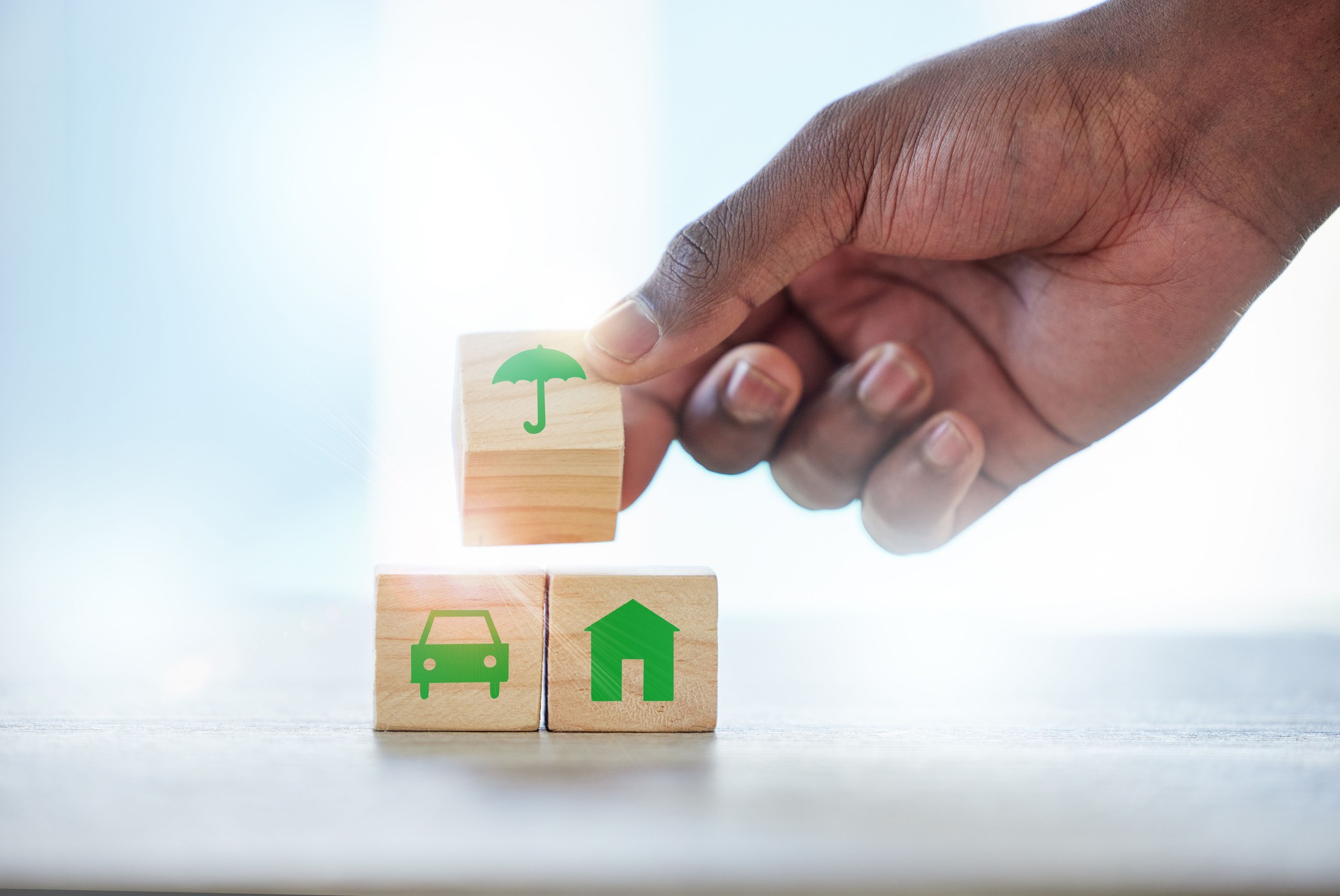 Shot of an unrecognisable man assembling wooden blocks with insurance related symbols on them